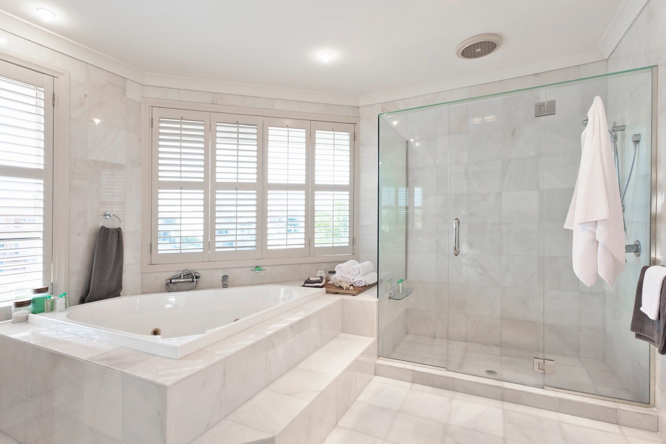 spacious accessible bathroom in whites and beiges with windows and shutters